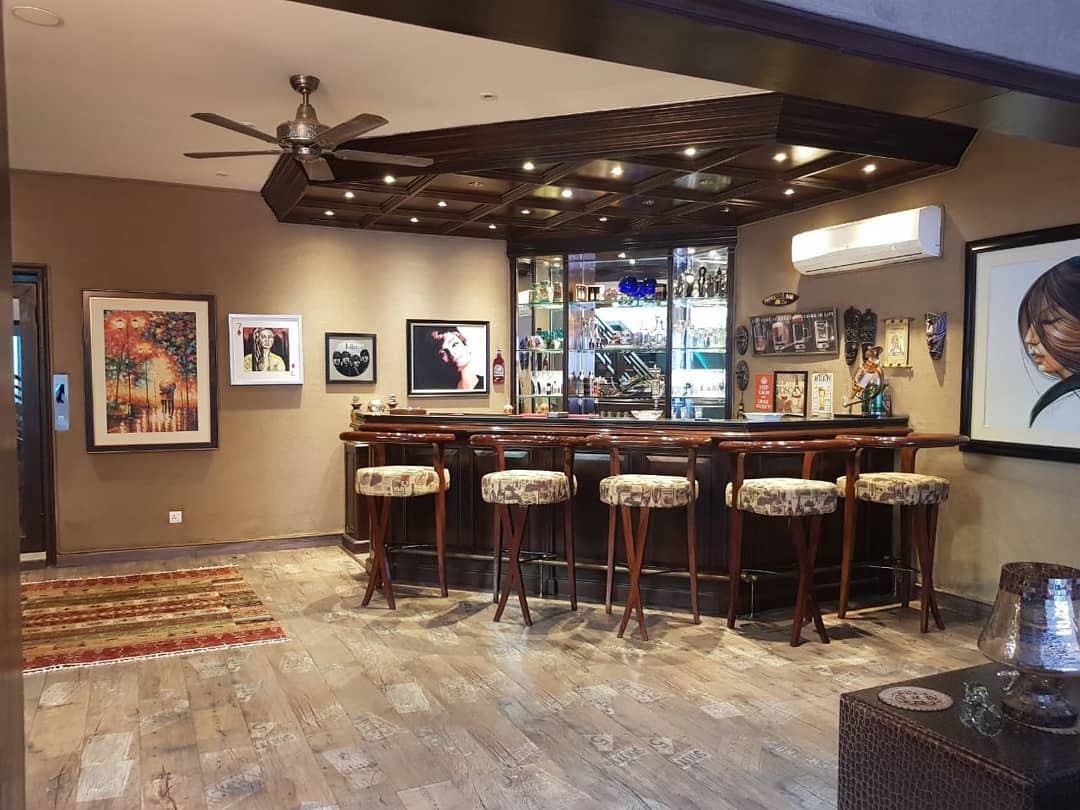 Stylish basement bar with wooden stools, glass shelves, and framed artwork on the walls.